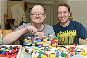 Mann mit Behinderung und Betreuer spielen zusammen Lego.
