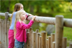 Zwei Kinder stehen hinter einem Zaun.