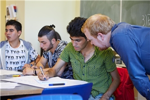 Deutschunterricht Flüchtlinge Drei Männer sitzen am Tisch, einer schreibt, ein anderer Mann scheint ihnen etwas zu erklären.