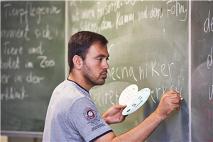 Flüchtling im Deutschunterricht Mann steht an Schultafel mit Kreide.