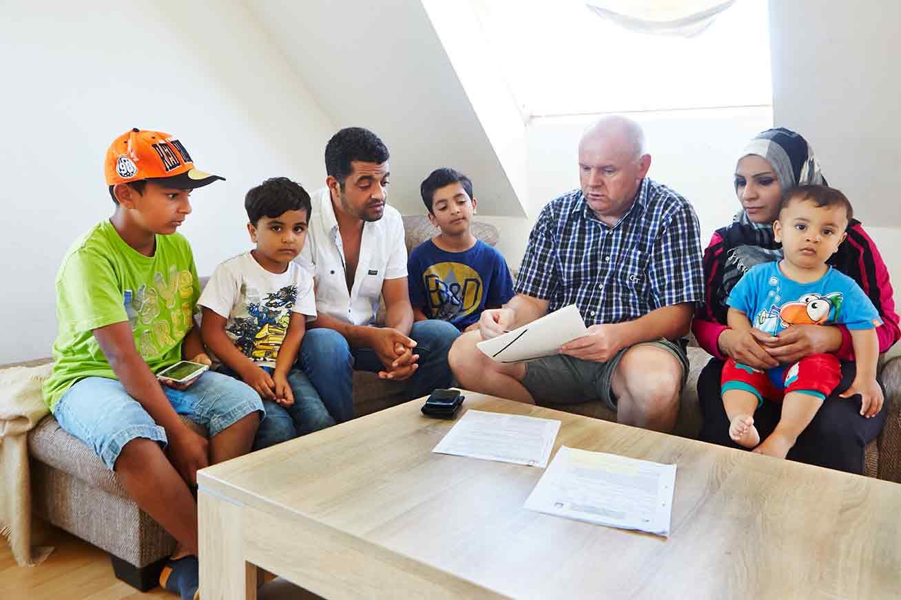 Eine sechsköpfige Familie sitzt mit einem Mann an einem Tisch, vor ihnen Papier.