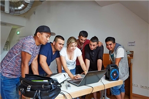 Eine Gruppe von Männern steht um eine Frau herum, die in den Laptop schaut.