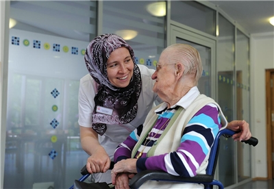 Frau mit Kopftuch als Pflegerin einer alten Frau im Rollstuhl
