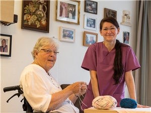 Eine Pflegerin mit einer strickenden Seniorin.