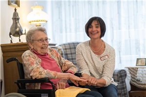 Eine Pflegerin spricht mit einer Seniorin und hält dabei ihre Hand.