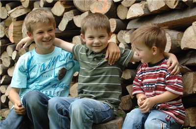 Drei kleine Jungs vor einem Stapel Holz