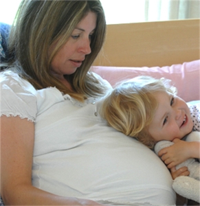 Ein kleines Mädchen schmiegt sich an seine schwangere Mutter 