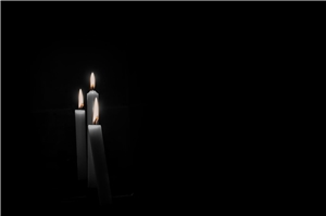 Drei brennende Kerzen vor schwarzem Hintergrund.