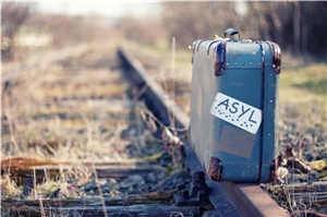 Koffer mit Aufdruck Asyl steht auf Eisenbahnschienen.