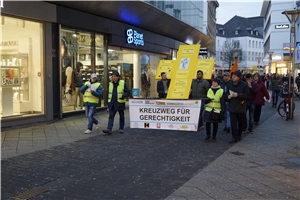 Eine Menschengruppe trägt ein großes gelbes Kreuz durch die Straßen Krefelds.