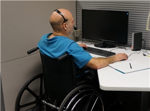 Mann im Rollstuhl mit Headset am Arbeitsplatz