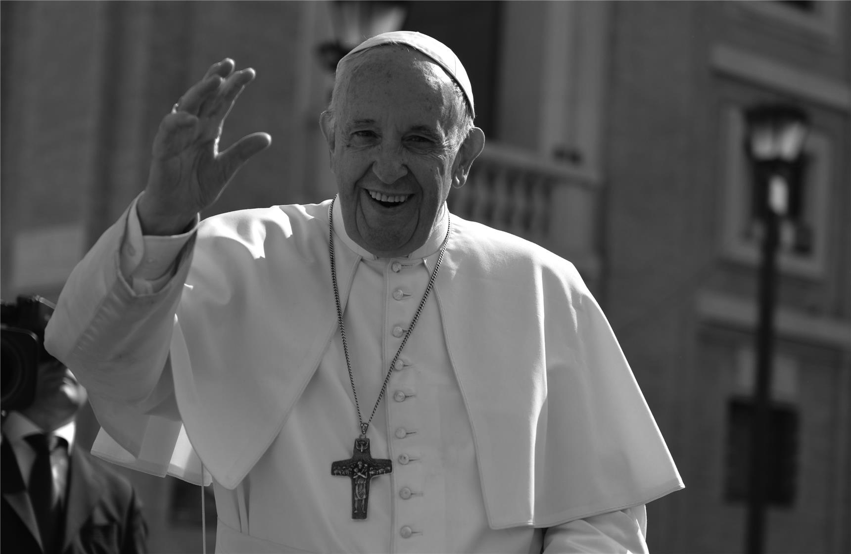 Der Papst in weißer Soutane winkt mit der rechten Hand.