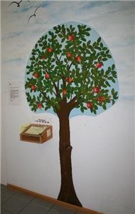 an die Wand gemalter Apfelbaum  links daneben in Hüfthöhe ein Holzkasten