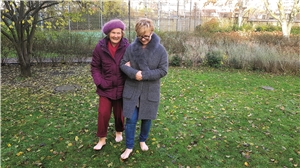 Kneipp - Spaziergang Zwei Damen mit warmen Jacken bekleidet, spazieren barfuß über eine grüne, herbstliche Wiese.