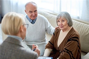 Eine Mitarbeiterin ist im Gespräch mit zwei Senioren in ihrer Häuslichkeit. Sie führt die Pflegeberatung durch.