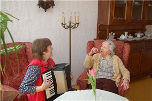 Caritas-Seniorenheim St. Albertus, Berlin-Hohenschönhausen Bewohnerin sitzt mit Angehöriger in gemütlicher Sitzecke. Angehörige spielt Akkordeon