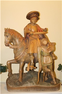 Wir sehen eine Holzschnitzerei. Auf einem Pferd sitze ein Mann dessen rechte Hand mit einem Schwert einen Mantel teilt. Vor dem Pferd steht ein armer Mann auf einem Bein und schaut hinauf. 