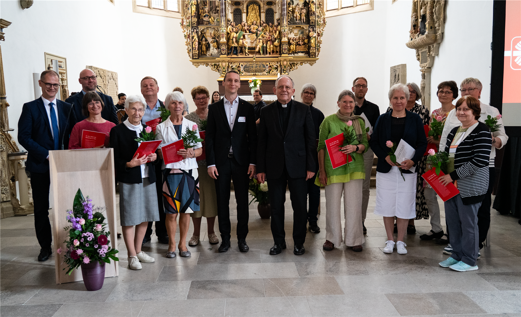 Zahlreiche Menschen stehen in zwei Reihen im Altarraum und lächeln in die Kamera