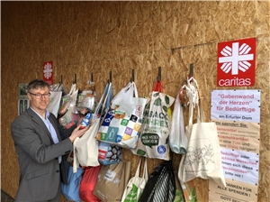 Caritasdirektor Wolfgang Langer steht an der „Gabenwand der Herzen“, die mit zahlreichen bunten Tüten voller Spenden bestückt ist