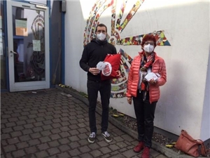 Karola Stange und ein Mitarbeiter des Erfurter Tagestreffs stehen vor dem Gebäude und übergeben FFP2-Masken