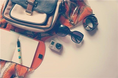 Tasche, Notizbuch mit Stift, Sonnenbrille, Kamera und Uhr auf Strandtuch