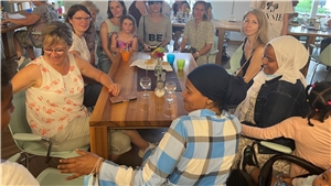 Eine Gruppe von Frauen und Kindern unterschiedlichster Nationen sitzen gemeinsam in einem Café an einem Tisch.