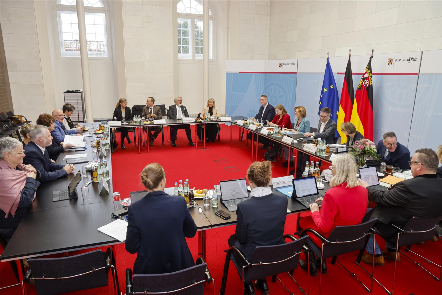 Jahresgespräch des LIGA-Vorstands mit dem rheinland-pfälzischen Kabinett tagt in einem großen Raum an Tischen die in der geschossenen U-Form stehen.