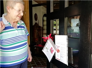 Eine ältere Dame steht an ihrer Haustüre und guckt auf Zettel die dort vom Ökumenischen Besuchsdienst angebracht wurden