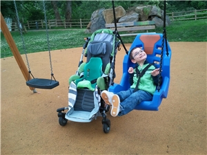 Kind mit Behinderung in behindertengerechter Schaukel, Rollstuhl steht daneben