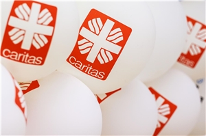 Wei�e Luftballons mit rotem Caritas-Flammenkreuz