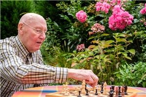 Ein Senior sitzt an einem Gartentisch und spielt Schach