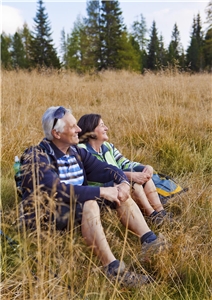Ein älterer Mann und eine Frau machen beim Wandern eine Pause in einem Feld