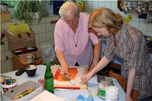 Blomenberg-Haus - Ergotherapie Eine Bewohnerin gestaltet eine Leinwand und wird dabei von einer jungen Mitarbeiterin unterstützt.