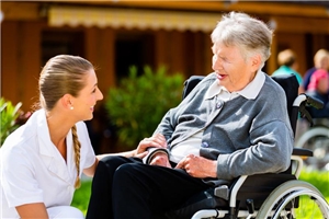 Eine Pflegerin kniet neben einer Seniorin im Rollstuhl