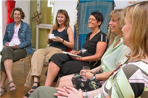 Das Foto zeigt eine Gruppe Frauen, die im Kreis sitzen und Freude miteinander haben.