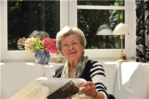 Eine ältere Dame sitzt am Fenster und liest Zeitung