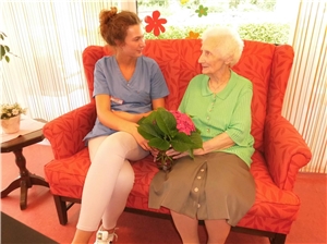 Eine Seniorin und eine Mitarbeiterin sitzen auf einem gemütlichen Sofa
