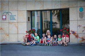 Eine Mutter und viele Kinder sitzen vor dem Eingang der Mutter-Kind-Klinik St. Ursula in Winterberg.