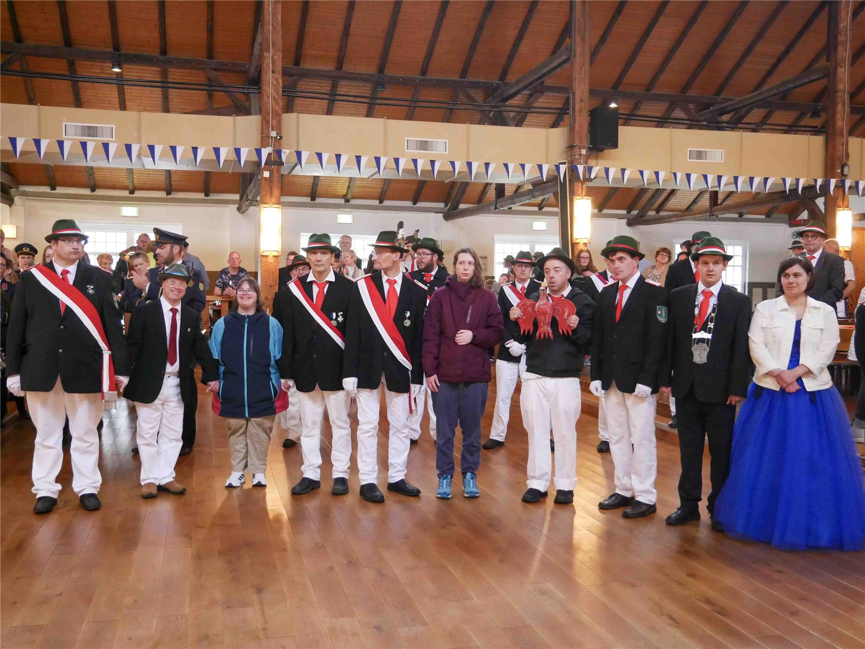 Zwei Schützenfestpaare feiern mit anderen Schützen in einer großen Halle.