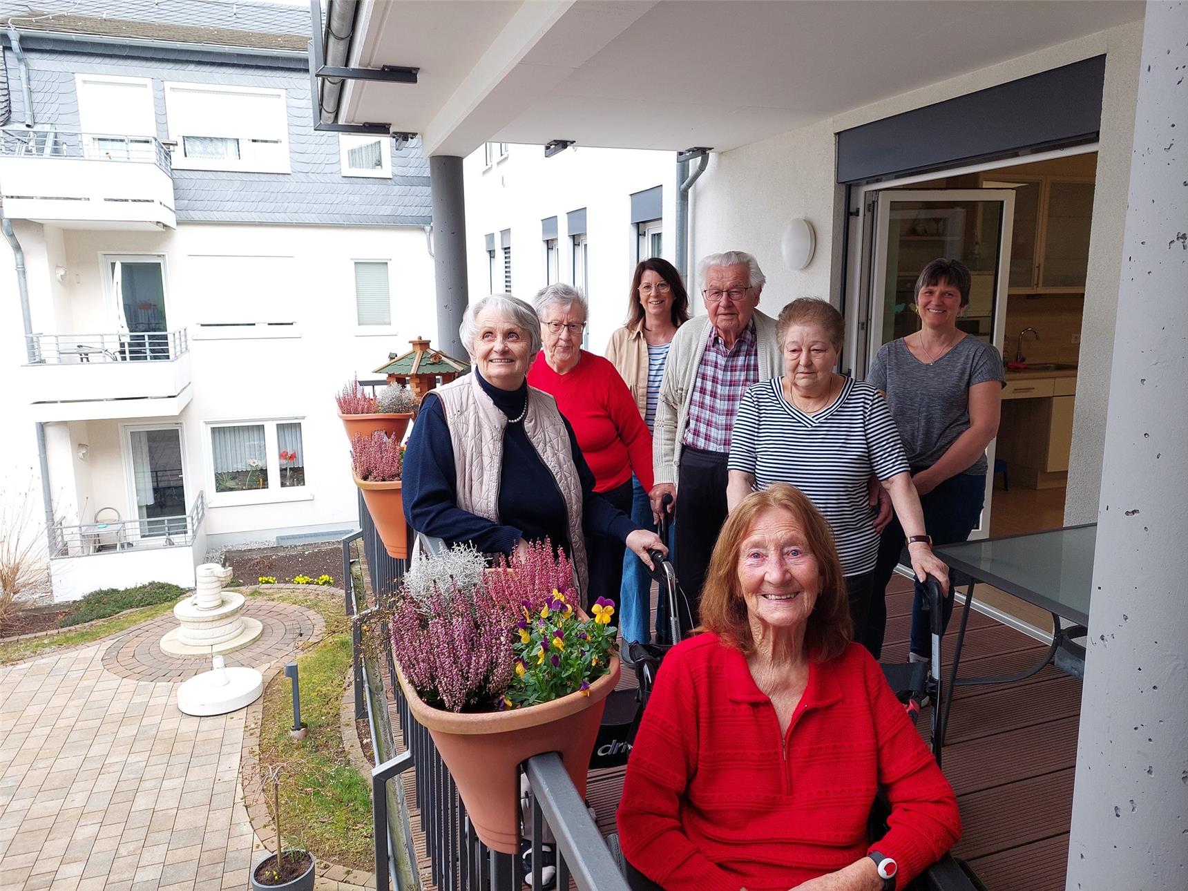 Sieben Frauen und ein Mann stehen auf einem Balkon und lachen in die Kamera.