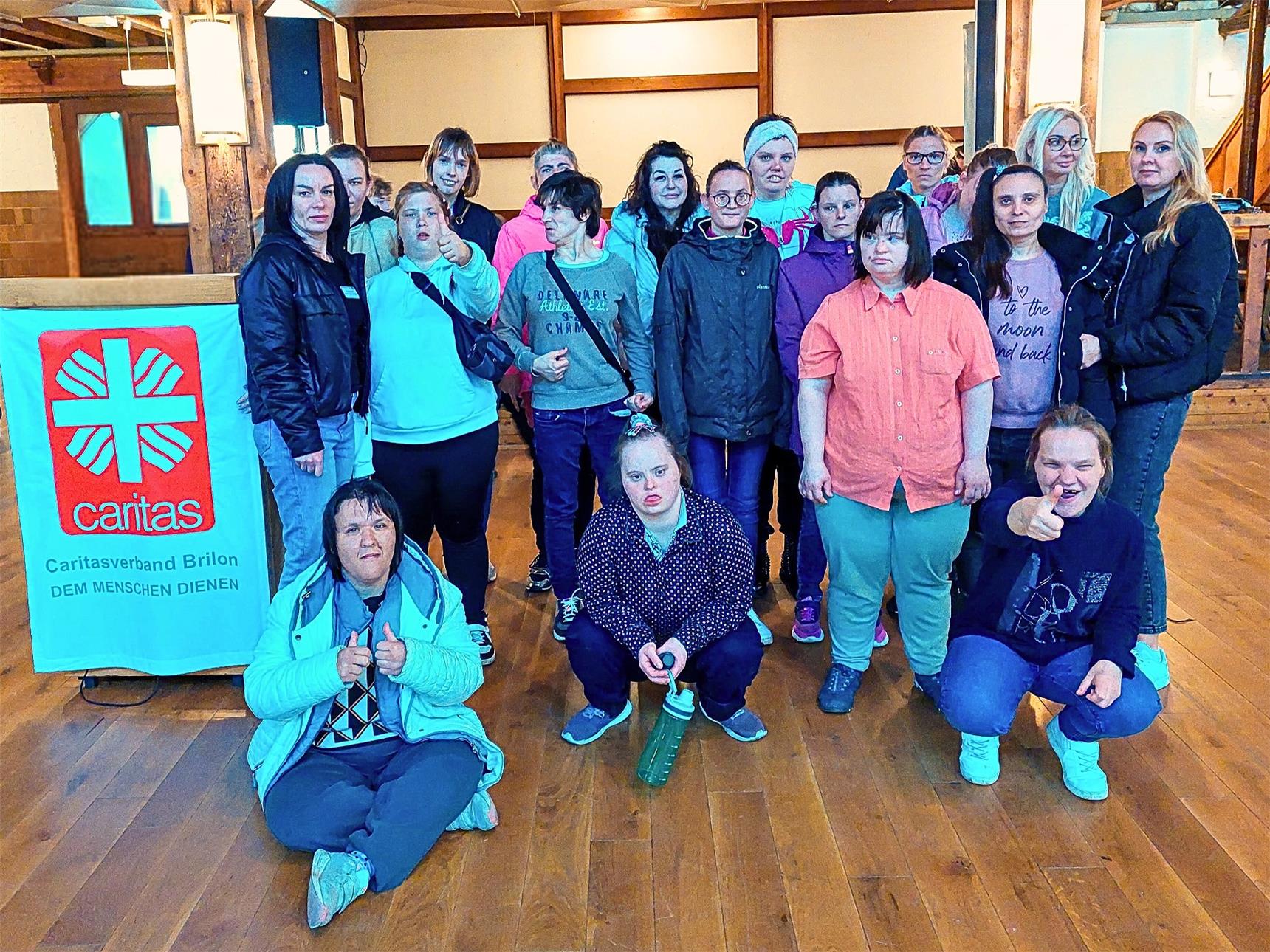 Eine Gruppe Frauen steht in einer großen Halle und lacht in die Kamera. 