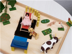 Holzbrett mit verschiedenartien Spielfiguren und Bauklötzen, auf dem ein Kind seine Familiensituation nachstellen kann
