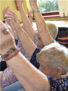Seniorinnen sitzen nebeneinander und nehmen an einer gymnastischen Übung teil