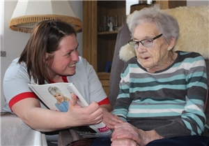 Pflegefachkraft bietet einer Seniorin eine Zeitschrift zum Lesen an