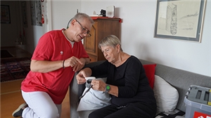 Ein Pfleger erklärt einer älteren Dame auf dem Sofa das Blutdruckgerät