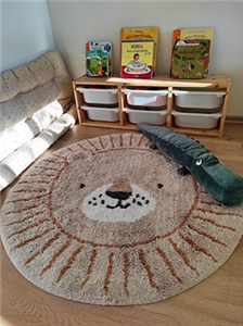 Foto eines Kinderzimmers, darin ein runder Teppich mit Löwengesicht, ein Stoffkrokodil und ein Regal mit Kinderbüchern und Spielsachen