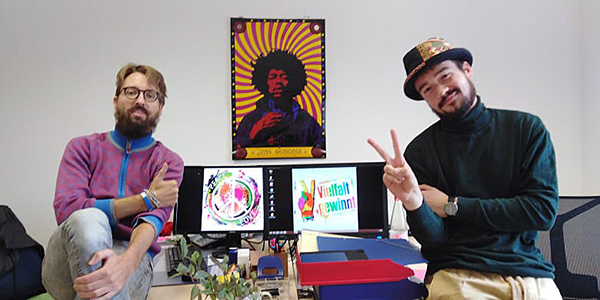 Zwei Männer neben bunten Bildern über Frieden und Vielfalt