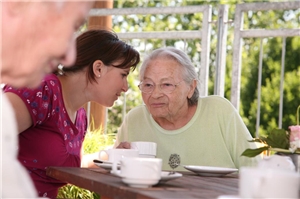Junge Frau am Kaffeetisch im Gespräch mit zwei älteren Damen