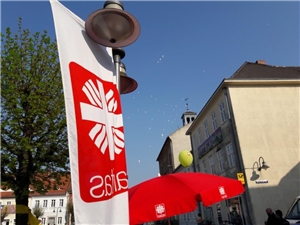 Caritas-Fahne mit rotem Flammenkreuz bei einer öffentlichen Veranstaltung.