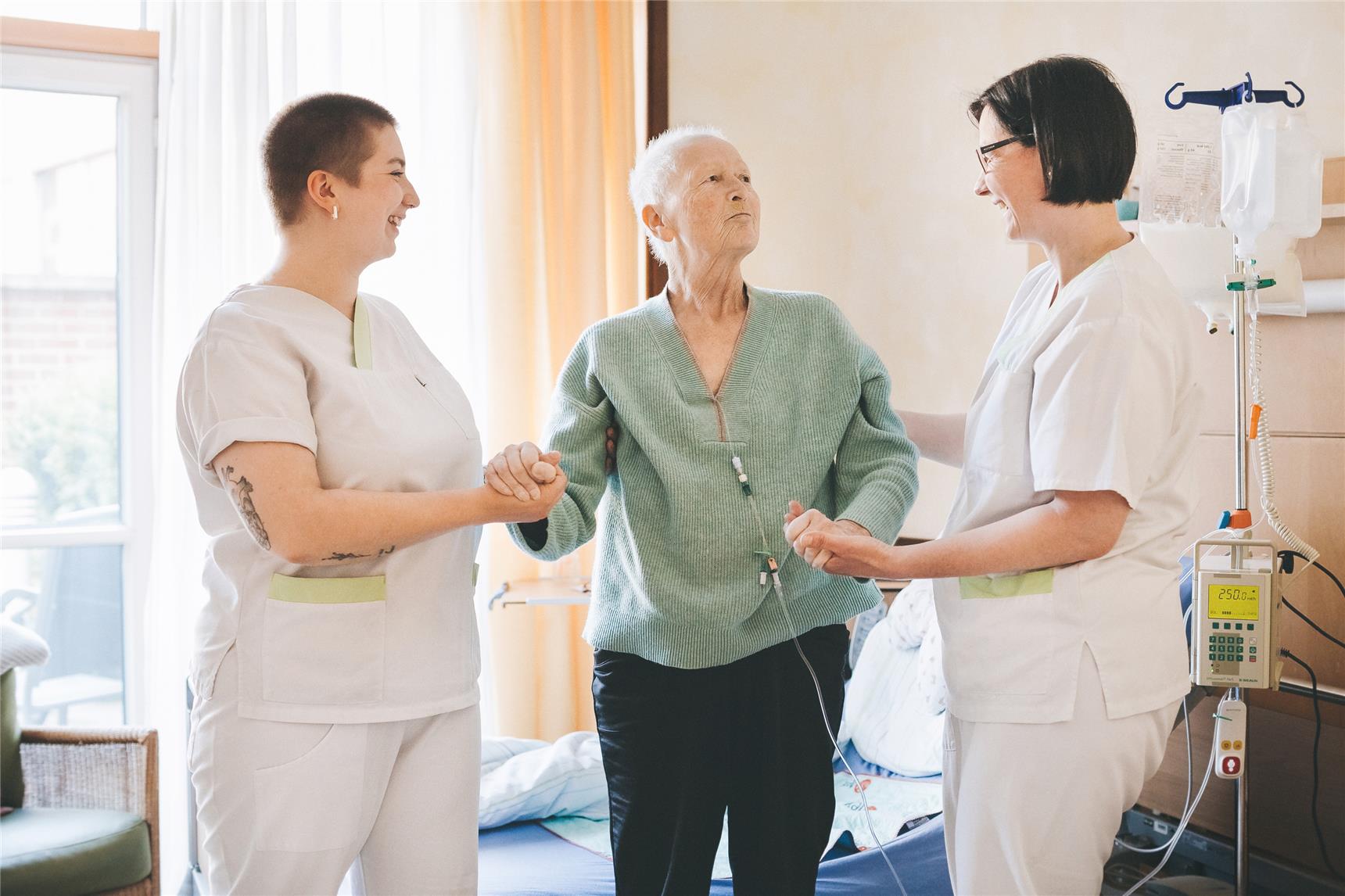 Zwei Pflegekräfte der Palliativstation stützen eine Patientin.